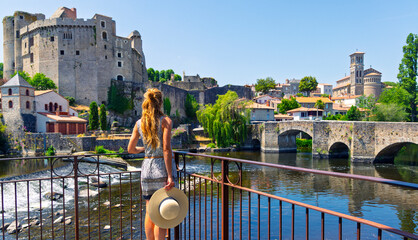 Woman traveler with straw hat looking at medieval castle and stone bridge in french town, Clisson © M.studio
