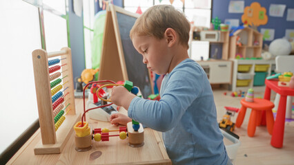 Fototapeta premium Boy threads colorful wooden beads on a bead maze and abacus with hands on a table in a playroom building; concentration early learning.