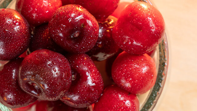 Close up of fresh ripe red cherries with water drops in a glass bowl on wooden background