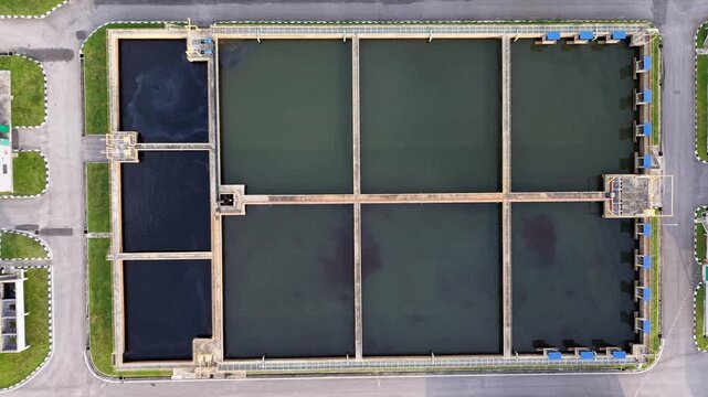 Aerial shot of rectangular water treatment basins divided into sections surrounded by roads and green grass, illustrating infrastructure for water purification and management.