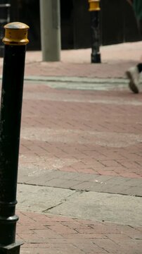 Vertical video: Framing bollard holding curb as people entering to cross, cyclist passing with bike