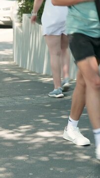 Vertical video: Walking adult in green top black shorts checking phone toward lens on shaded path