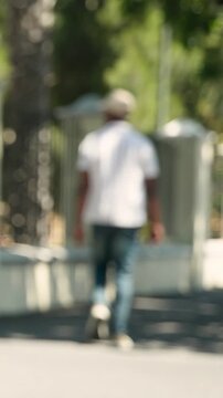 Vertical video: Entering frame, man in light shirt and cap walking down park path, passing bicycle