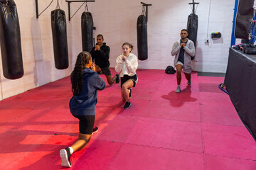 Fototapeta premium Diverse training group performing lunges in sportswear on foam tiles at boxing ring with heavy bags