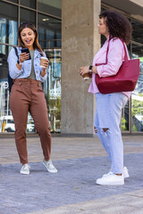 African American women standing and talking at glass entry holding phone, coffee cups, maroon bag © wavebreak3