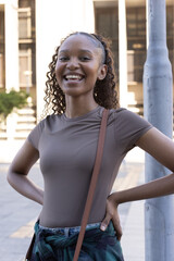 African woman posing smiling in plaza wearing taupe top, plaid shirt tied, bag strap visible © wavebreak3