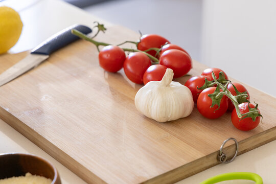 Cherry tomatoes on vine and whole garlic bulb sitting on wooden cutting board, knife resting
