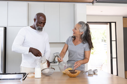 Diverse senior couple preparing breakfast at home kitchen island with glass bowls and sieve