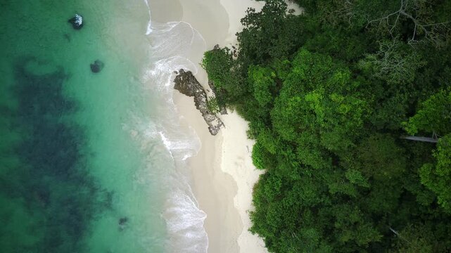 Aerial view of a serene beach with turquoise water, white sand, and lush greenery in Teluk Ijo, Banyuwangi, East Java, Indonesia.