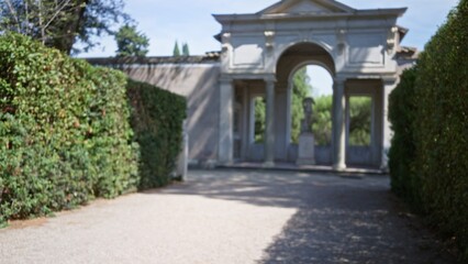 Obraz premium Blurred garden path with classical stone arch and trimmed hedges, defocused; background backdrop copyspace calm.