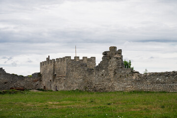 the stone fortification walls and ramparts of an ancient castle, set against a backdrop of an overcast sky and an expansive green field. © Andrey