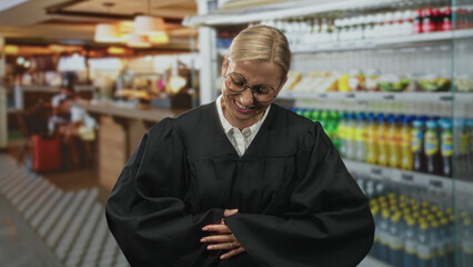 Fototapeta premium Woman judge clutching stomach in building wearing black robe and glasses while grimacing and holding hands over belly; discomfort urgency.