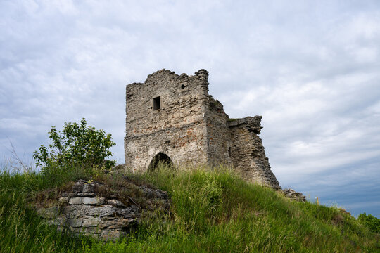 the solitary, weathered stone ruins of an ancient tower standing atop a lush, grassy hill under an overcast sky