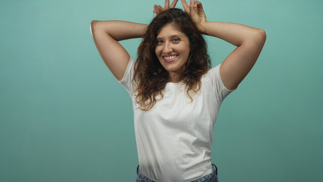 Woman wearing white t shirt with hands making bunny ears, bare arms visible, smiling in a mint studio; joy spontaneity energy.