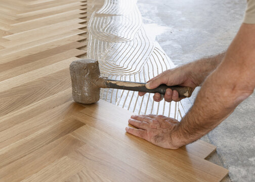Worker installing herringbone parquet flooring with rubber mallet during hardwood floor installation