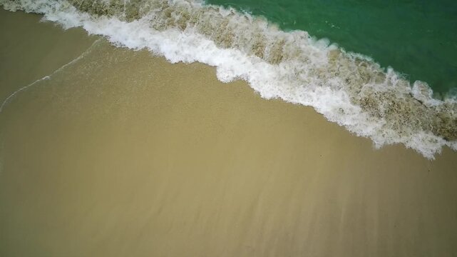 Aerial view of waves gently lapping onto the sandy shore of Teluk Ijo in Banyuwangi, East Java, Indonesia, with a green ocean background.