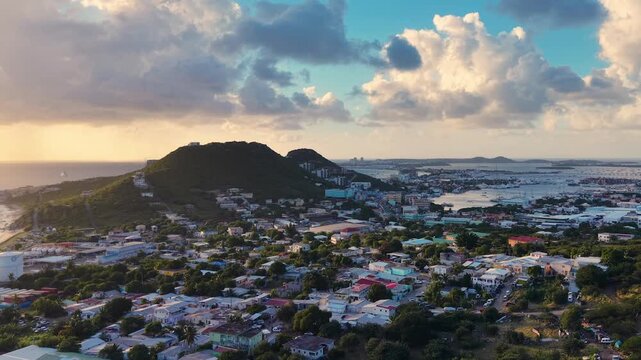 Aerial view of Cole Bay town and hills on the Dutch side of Sint Maarten island. Panoramic coastal landscape of the Caribbean destination under a cloudy sky. Simpson Bay Lagoon with boats.