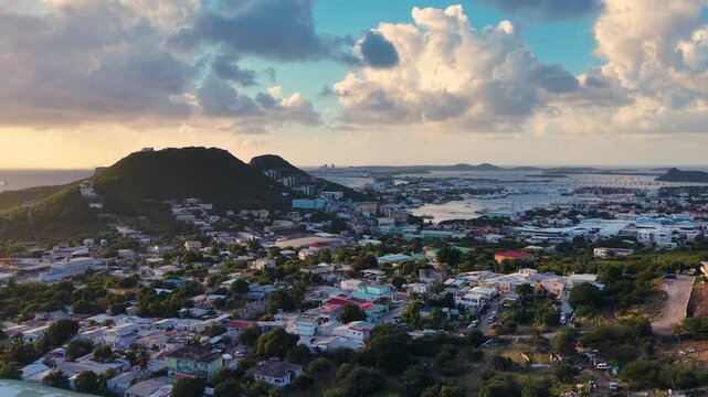 Aerial view of Cole Bay town and hills on the Dutch side of Sint Maarten island. Panoramic coastal landscape of the Caribbean destination under a cloudy sky. Simpson Bay Lagoon with boats.