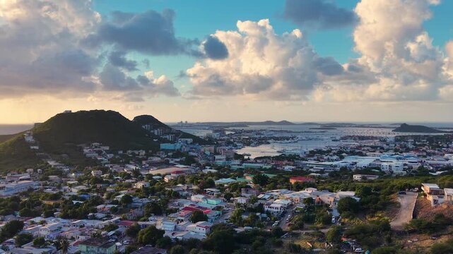Aerial view of Cole Bay town and hills on the Dutch side of Sint Maarten island. Panoramic coastal landscape of the Caribbean destination under a cloudy sky. Simpson Bay Lagoon with boats.