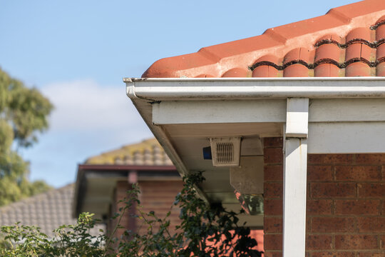 Roof gutter, terracotta tiles and brick eave on suburban Australian home.&nbsp;Suburban housing construction details relevant to home maintenance&nbsp;showing a PVC roof gutter, a subfloor vent