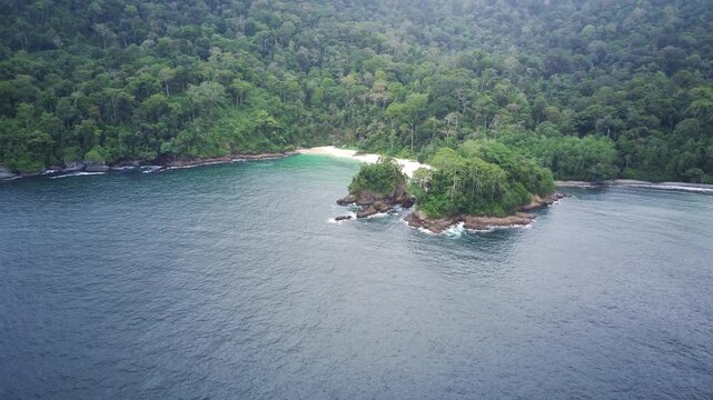 Aerial view of a small island with lush greenery and a white sandy beach in Teluk Ijo, Banyuwangi, East Java, Indonesia, surrounded by calm blue waters and dense forest.