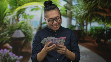 Fototapeta premium Man counting indonesian rupiah banknotes with hands in forest setting, looking down; savings prosperity contentment.