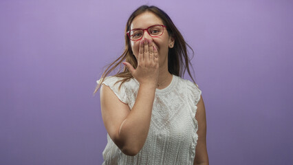 Fototapeta premium Young woman covering mouth with hand wearing red glasses and white blouse in purple studio; surprise.