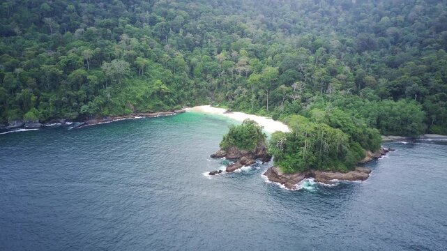 Aerial view of a serene island with lush greenery and a white sandy beach surrounded by calm blue waters in Teluk Ijo, Banyuwangi, East Java, Indonesia.
