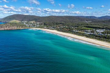 Fototapeta premium Aerial scene capturing Boomerang Beach near Pacific Palms, NSW, Australia, with residential homes and native bushland visible in the background. The sandy shoreline, clear ocean waters and landscape.