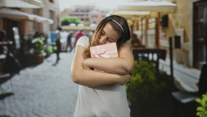 Fototapeta premium Woman hugging pink gift present on street with arms wrapped around box in affectionate hold; tenderness celebration.