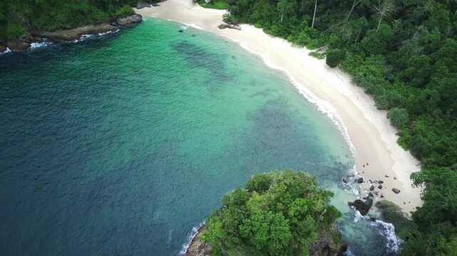Aerial view of a serene beach with turquoise water and lush greenery in Teluk Ijo, Banyuwangi, East Java, Indonesia.