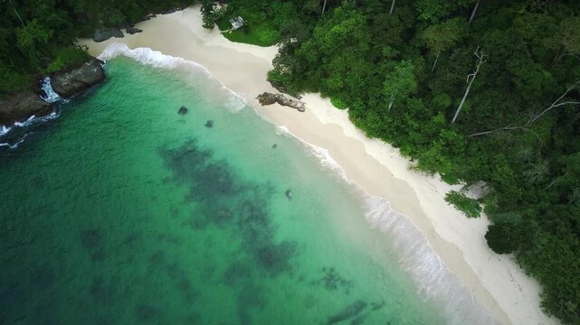Aerial view of a serene beach with turquoise water and lush greenery in Teluk Ijo, Banyuwangi, East Java, Indonesia.