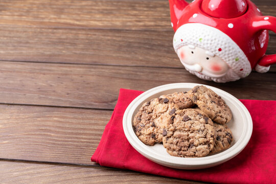 Chocolate chip cookies in a plate with Santa Claus teapot over wooden table with copy space