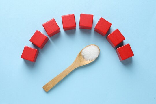 Diabetes control. Empty wooden cubes and spoon with sugar on light blue background, flat lay