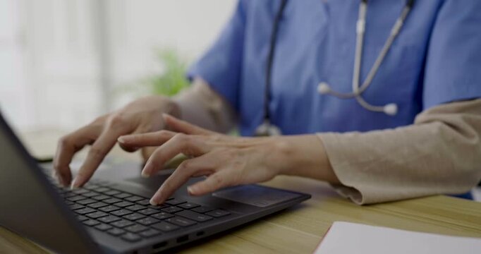 Close-up of a healthcare professional in medical scrubs typing on a laptop, representing digital healthcare, patient records, and telemedicine services.