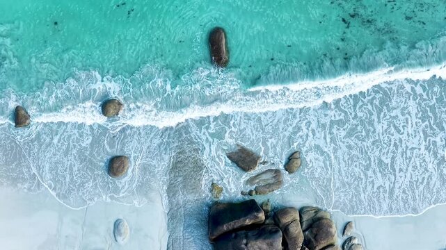 Faszinierende Drohnenaufnahme vom Plage de Boutrouilles: T&uuml;rkisblaues Wasser und wei&szlig;er Gischt-Schaum treffen auf hellen Sandstrand und markante, dunkle Granitfelsen.