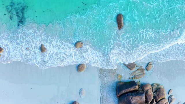 Faszinierende Drohnenaufnahme vom Plage de Boutrouilles: T&uuml;rkisblaues Wasser und wei&szlig;er Gischt-Schaum treffen auf hellen Sandstrand und markante, dunkle Granitfelsen.