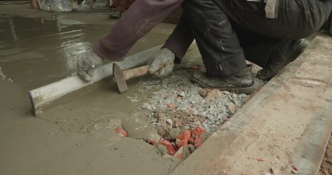 Close-up shot of a construction worker using a straightedge to level freshly poured liquid concrete, smoothing the wet cement surface to create a flat floor during a renovation project