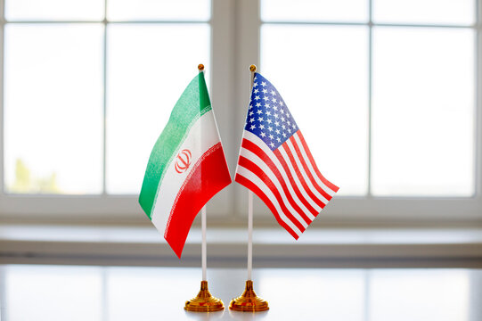 Iran and USA flags signal diplomatic negotiations. Two national banners on a bright desk imply talks, policy dialogue and an agreement for editors. Symbolic image of international diplomacy.