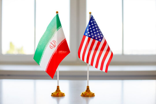 Flags USA Iran diplomacy negotiations conflict talks relations. Two desk flags on gold stands in bright light show bilateral dialogue and foreign policy. Clear concept of diplomacy and talks.