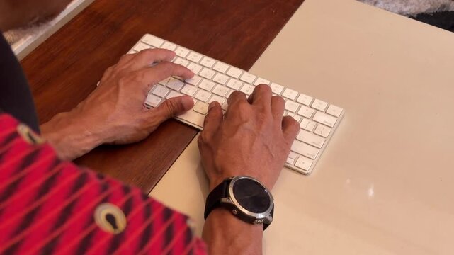 Shoulder close up shot showing old asian male typing on modern computer wireless keyboard, expressing busy activity