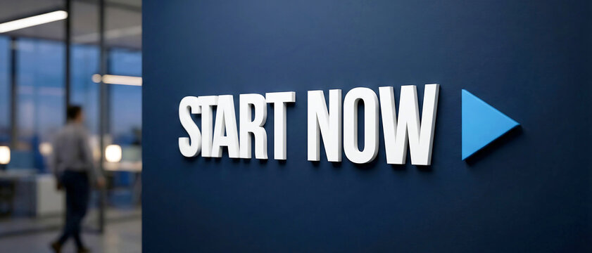 Large white three dimensional letters spelling start now with a bright blue play button icon attached to a dark navy blue wall in modern office