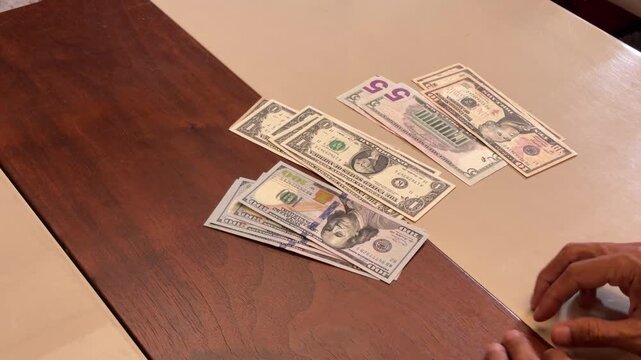 Asian male counting and sorting US dollar money bills on wooden table, expression of saving, life style, economy, payment, business