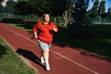 Obraz premium Curvy woman embraces fitness with joy while jogging on a sunny outdoor track