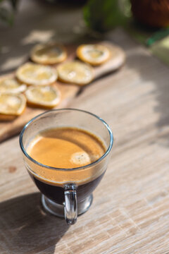 Glass cup of fresh espresso coffee on wooden table with blurred dried lemons on background