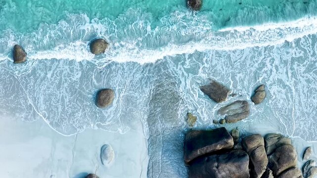 Faszinierende Drohnenaufnahme vom Plage de Boutrouilles: T&uuml;rkisblaues Wasser und wei&szlig;er Gischt-Schaum treffen auf hellen Sandstrand und markante, dunkle Granitfelsen.