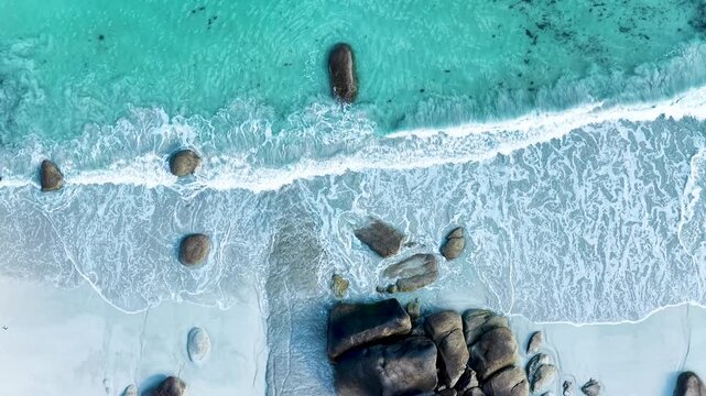 Faszinierende Drohnenaufnahme vom Plage de Boutrouilles: T&uuml;rkisblaues Wasser und wei&szlig;er Gischt-Schaum treffen auf hellen Sandstrand und markante, dunkle Granitfelsen.