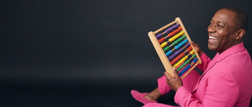 Black businessman holding colorful abacus counter wearing pink suit on dark background, smiling and laughing with copy space for financial calculations, business math education and creative budgeting.
