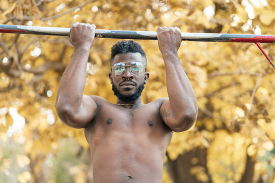 Muscular man doing pull-ups outdoors with autumn foliage in the background