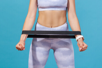Naklejka premium Cropped shot of woman in white sports top standing with elastic rubber expander on hands isolated over blue background
